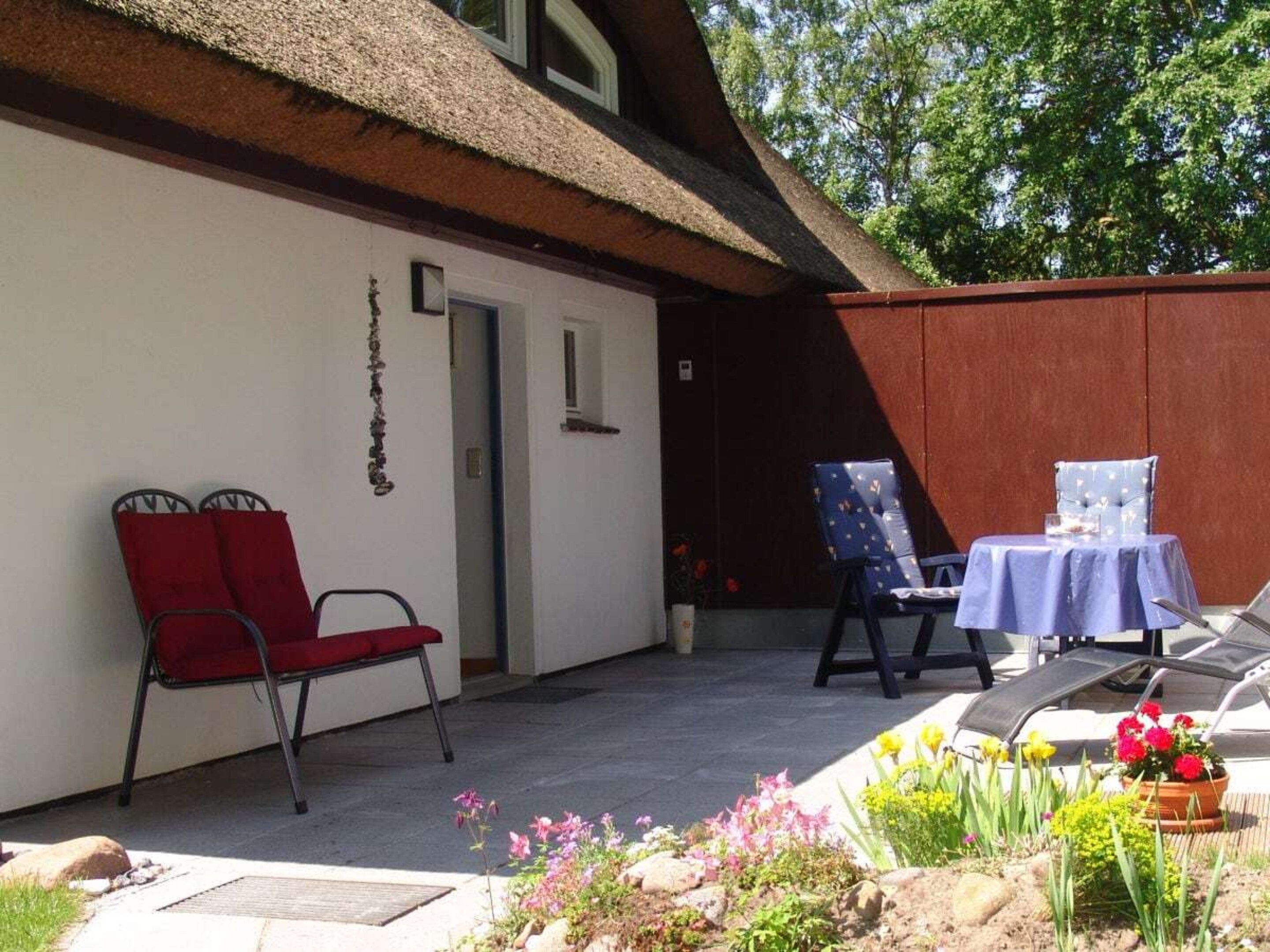 A patio with a red chair, a blue table, and a garden area with flowers and plants.