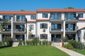 Un edifici residencial modern de diverses plantes amb balcons, teulada plana i gespa ben cuidada.