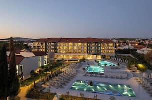 Un hotel con varias piscinas, un jardín ajardinado y vistas del entorno.