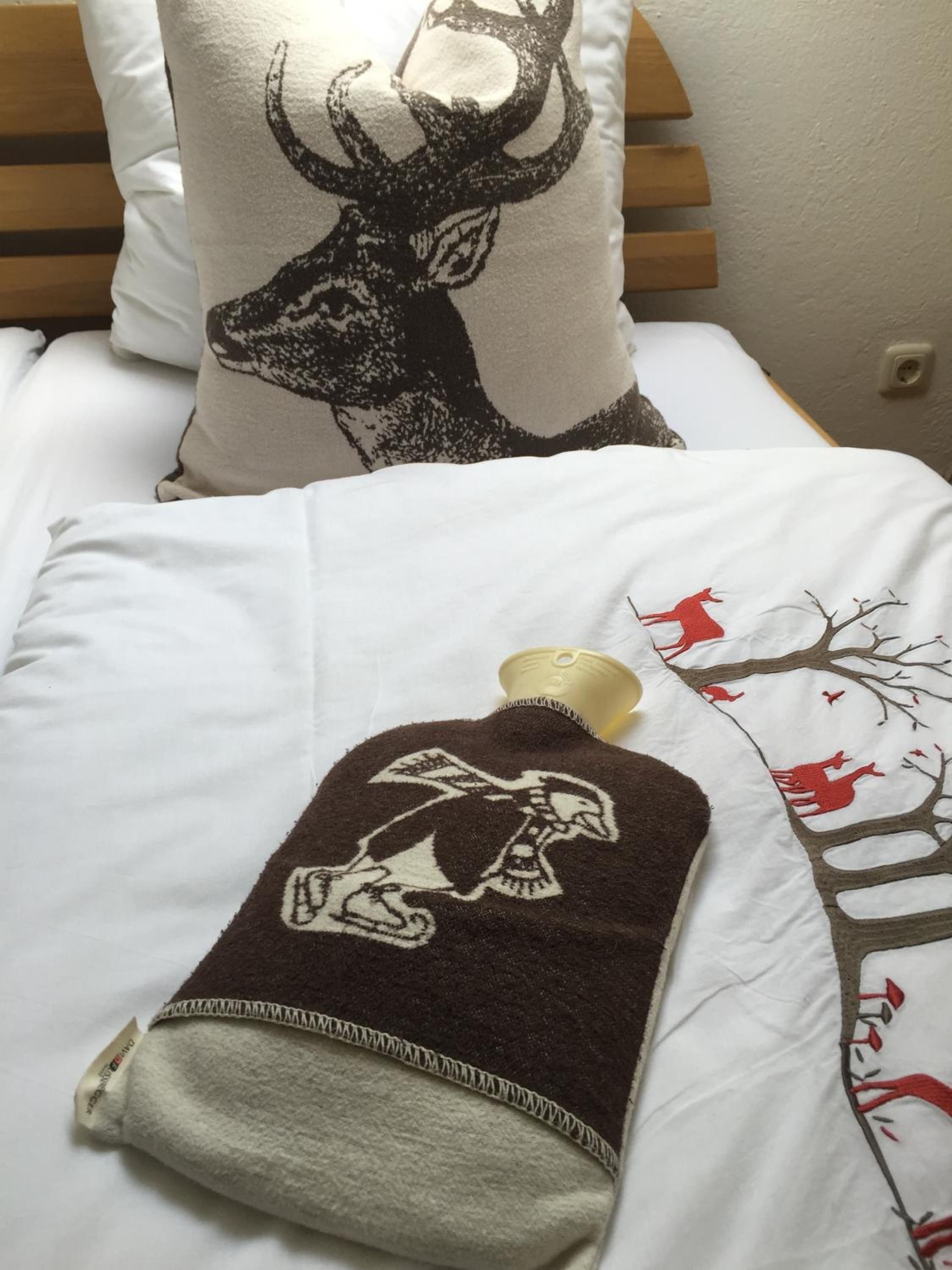 Un lit avec une literie blanche, une couverture marron ornée d’un motif blanc brodé, et un oreiller illustré d’un cerf en noir et blanc.