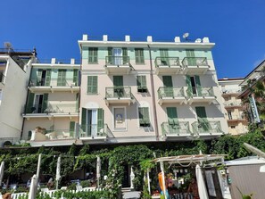 A multi-story building with balconies, a covered outdoor seating area, and a clear blue sky. - Hotel Eden Alaxi Hotels (Alassio)