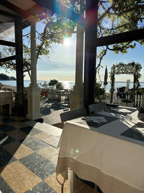 An outdoor dining area with tables set for guests, overlooking a beach with a clear view of the sea. - Hotel Eden Alaxi Hotels (Alassio)