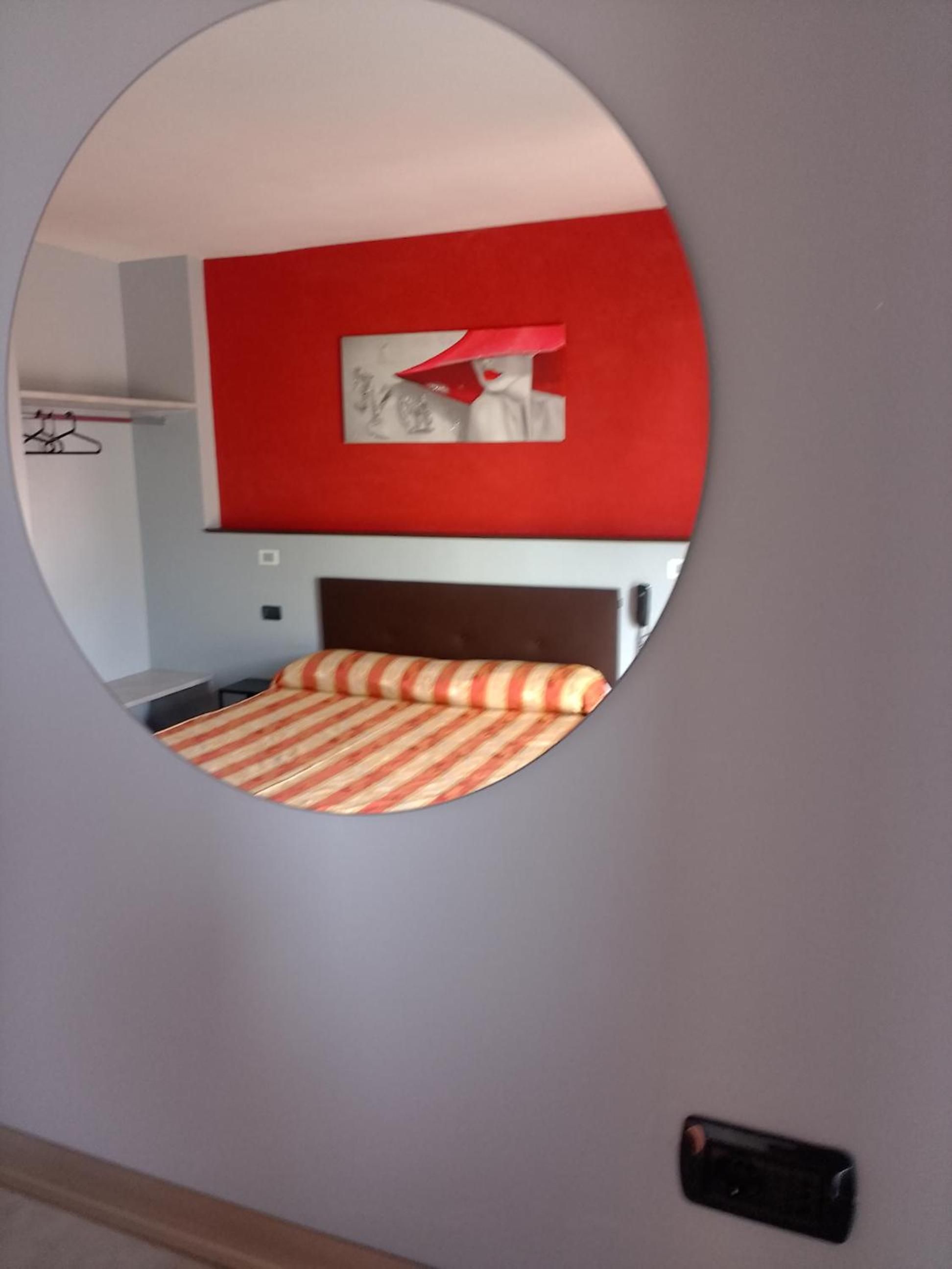 Ein Zimmer mit einem Bett, einer roten Wand und einem Spiegel, der Bett und Wand reflektiert.