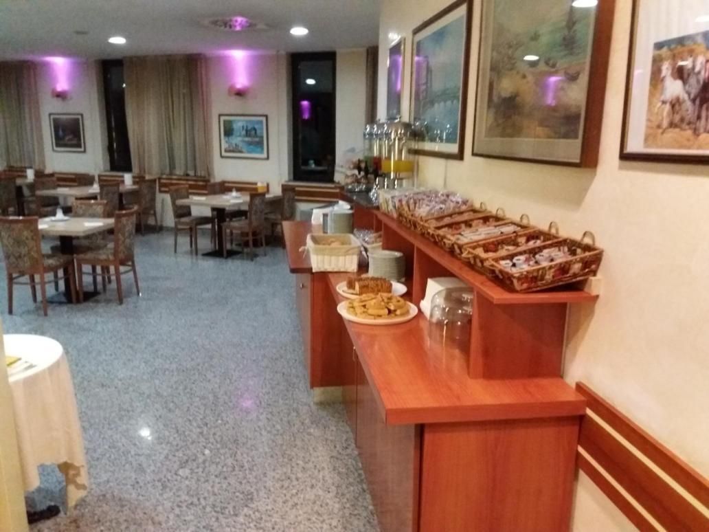 Ein Speisebereich eines Hotels mit Holztischen und -stühlen, einer Buffettheke mit Speisen sowie gerahmten Bildern an den Wänden.