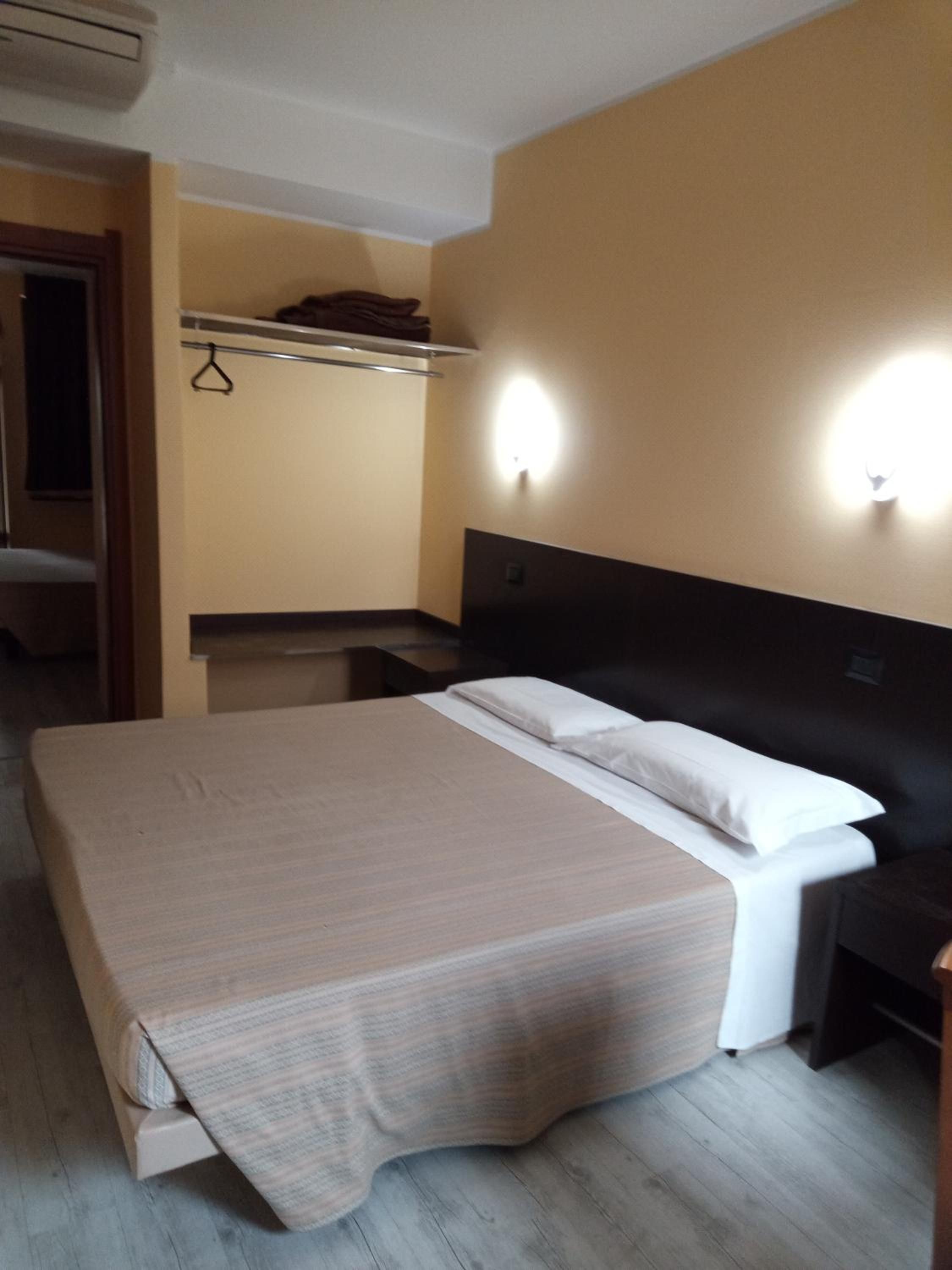 Habitació d'hotel amb llit, taules de nit, armari i mirall.