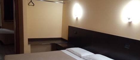 Habitació d'hotel amb llit, taules de nit, armari i mirall.