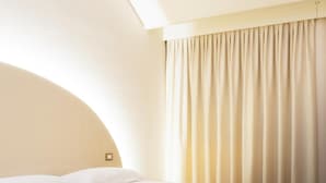 Ein Hotelzimmer mit einem Einzelbett, einem Kopfteil, einem Fenster mit Vorhängen und einem Teppichboden.
