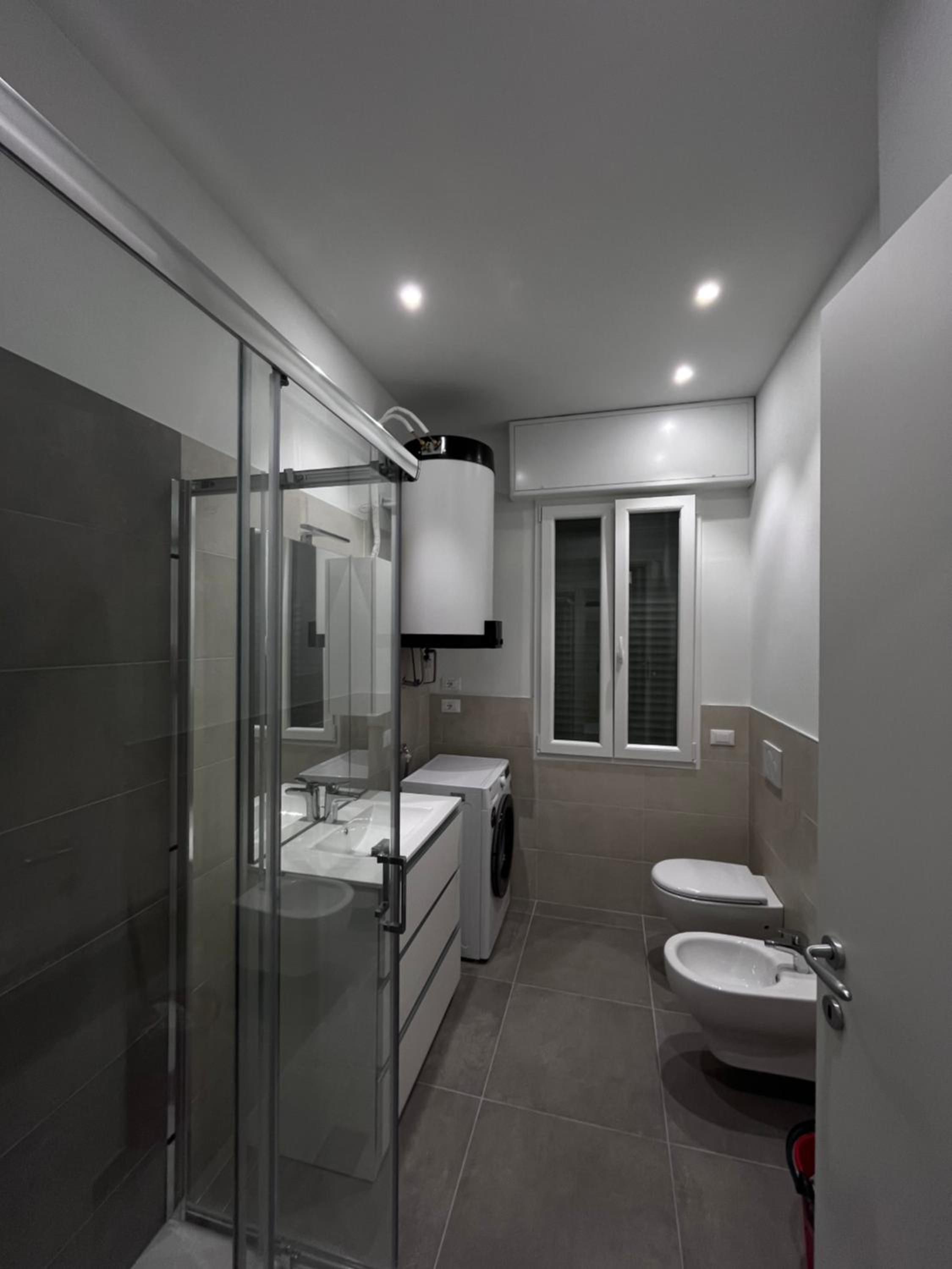 A modern bathroom with a glass shower enclosure, a built-in sink, a toilet, and a bidet.