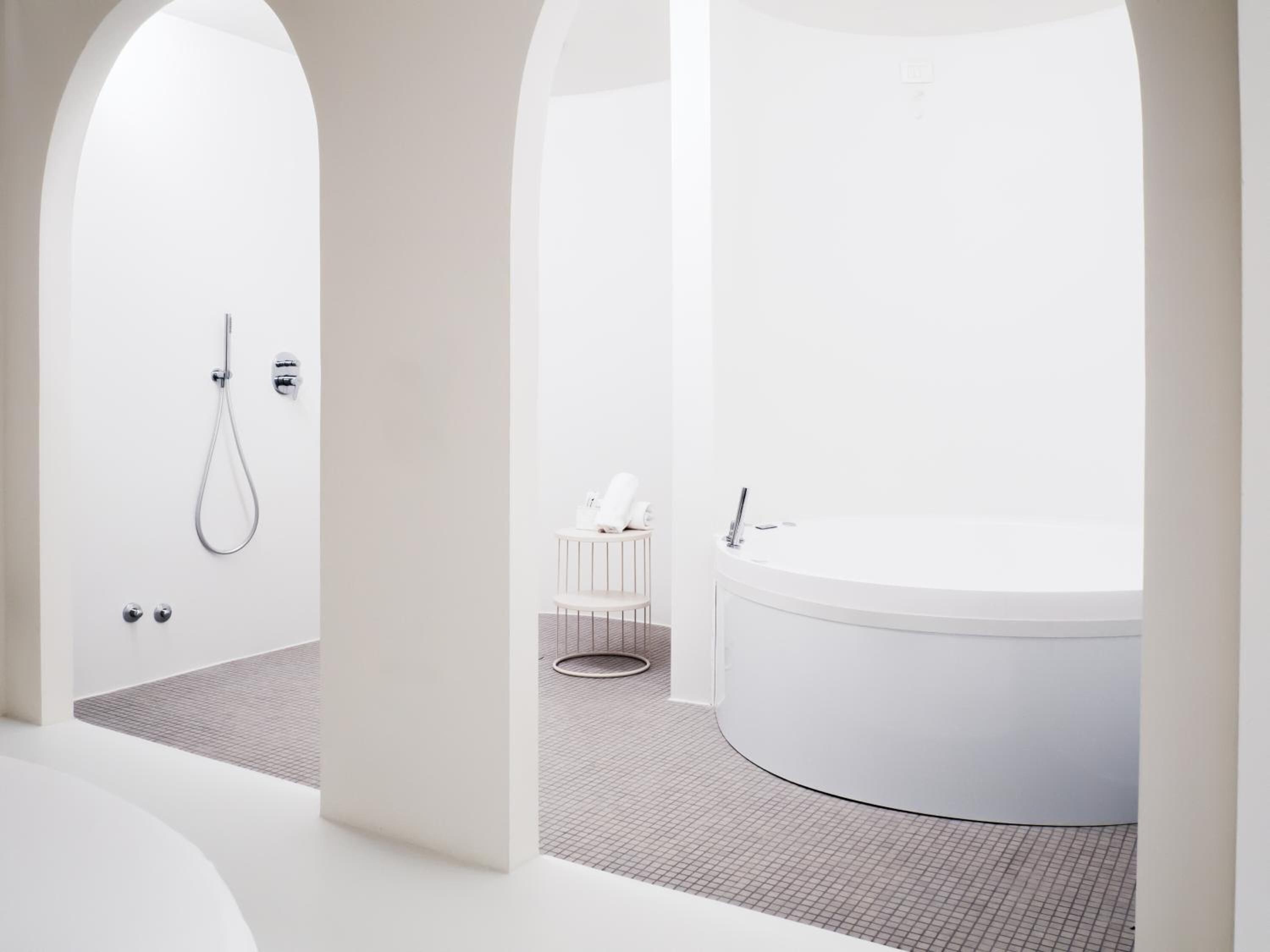 A modern bathroom with a freestanding bathtub, a shower, and a small seating area.