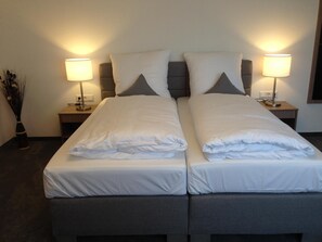 A double bed with white linens, two bedside lamps, and a vase of dried plants. - Tankbar's Hotelchen (Heroldsberg)