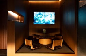 Una habitación con televisión montada en la pared, una pequeña mesa con sillas y un jarrón con flores.