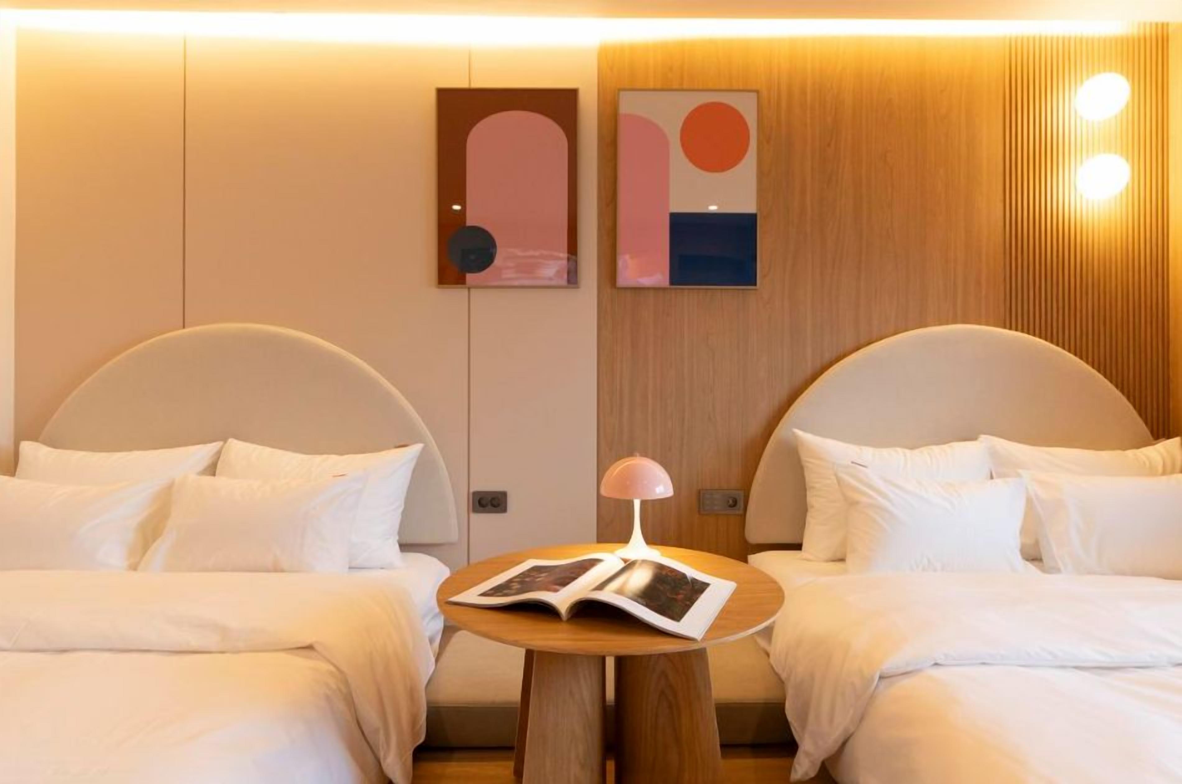 Habitación de hotel con dos camas, una mesita de noche con lámpara y una obra de arte en la pared.
