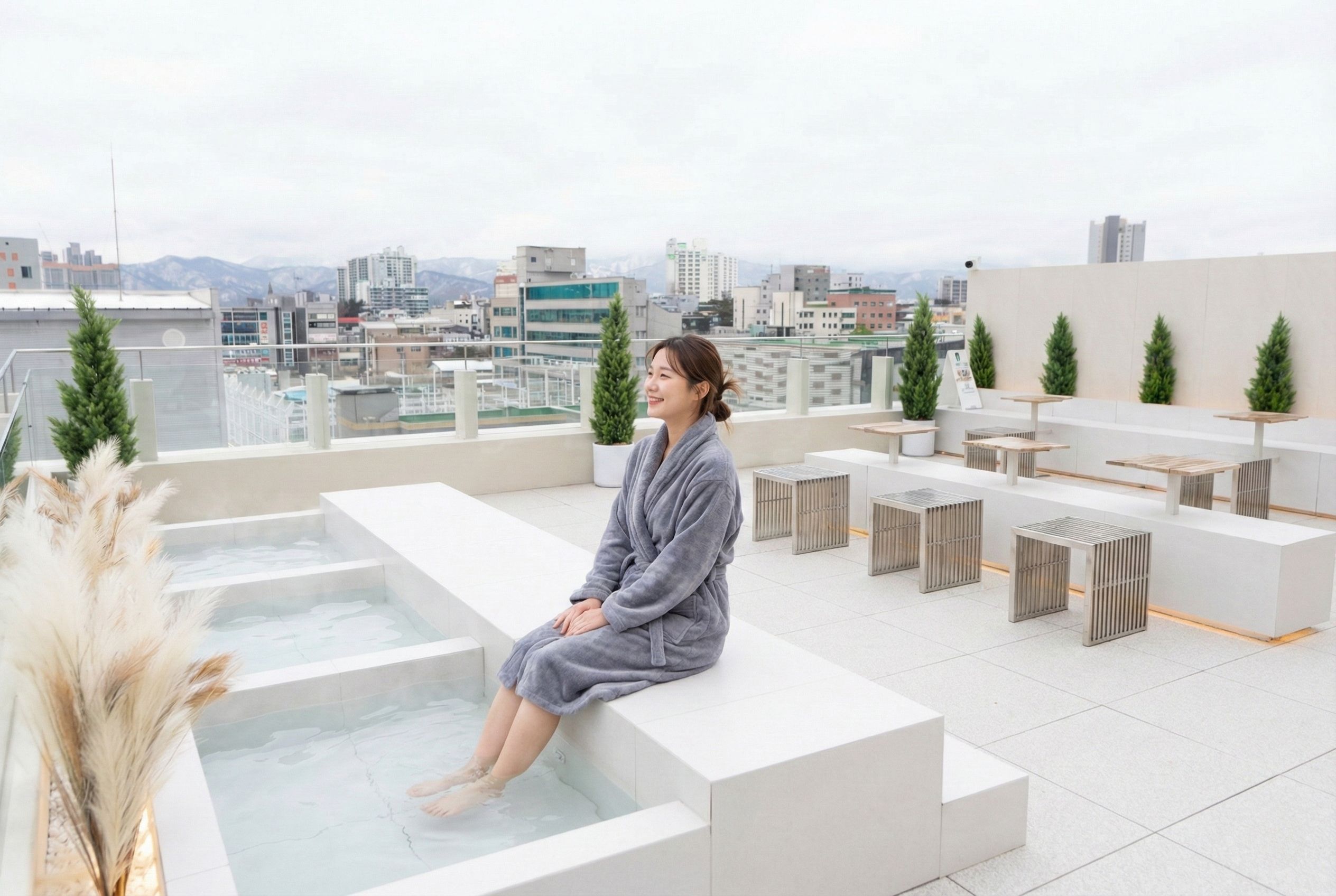 A person sitting by a spa tub on a rooftop terrace with a cityscape view.
