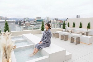 A person sitting by a spa tub on a rooftop terrace with a cityscape view.