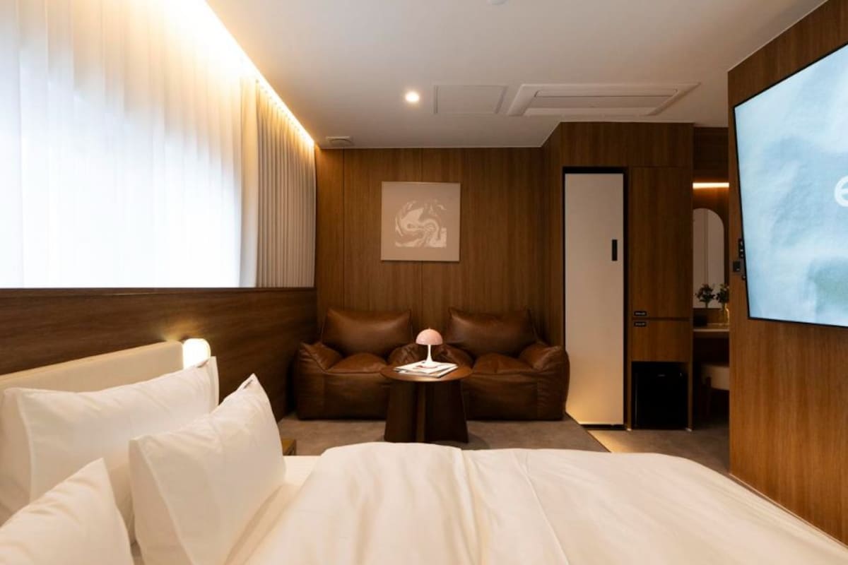 A hotel room with a bed, a seating area with a table, a television, and a door leading to a bathroom.