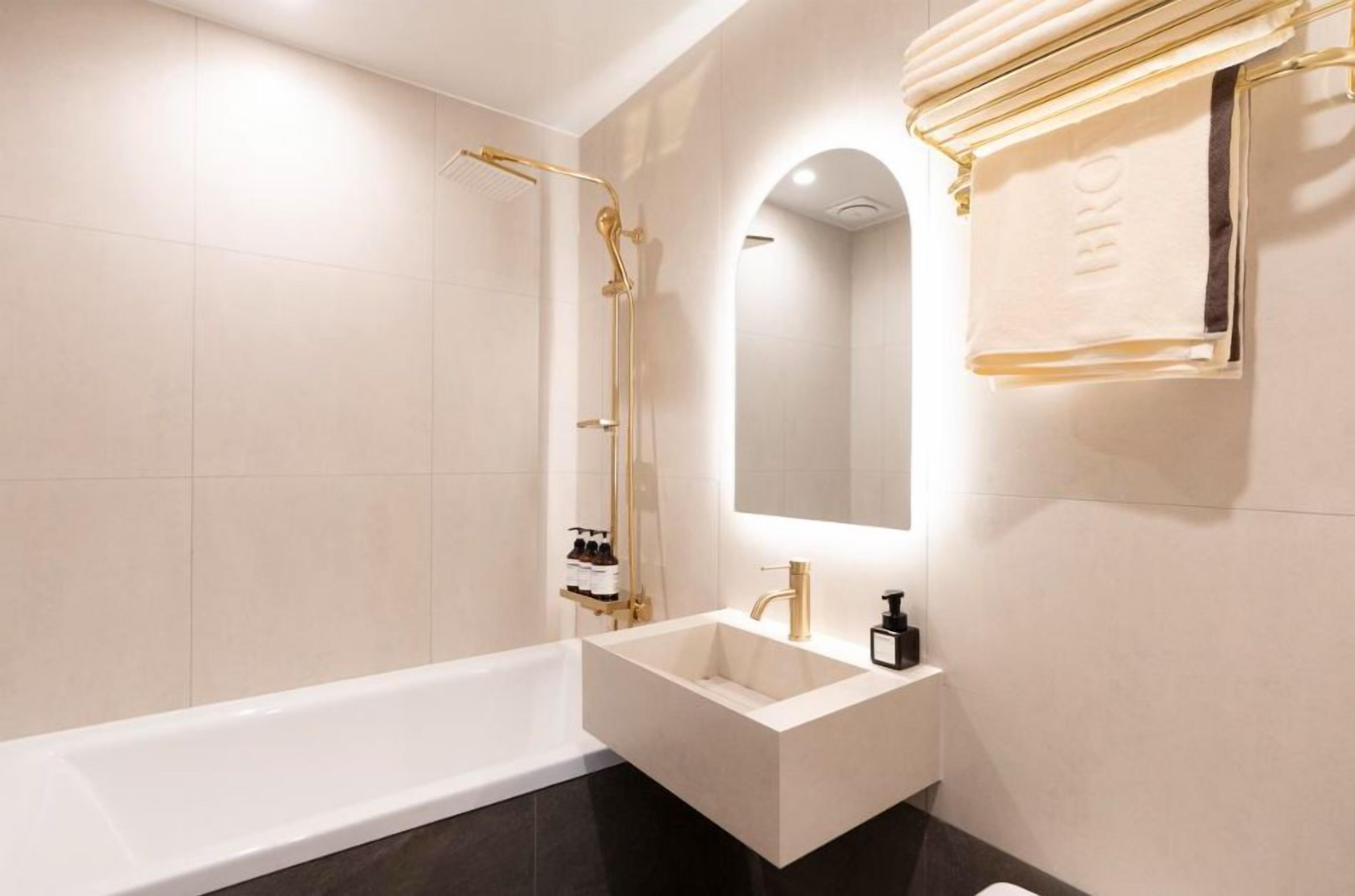 A modern bathroom with a freestanding bathtub, a gold showerhead, and a large mirror.