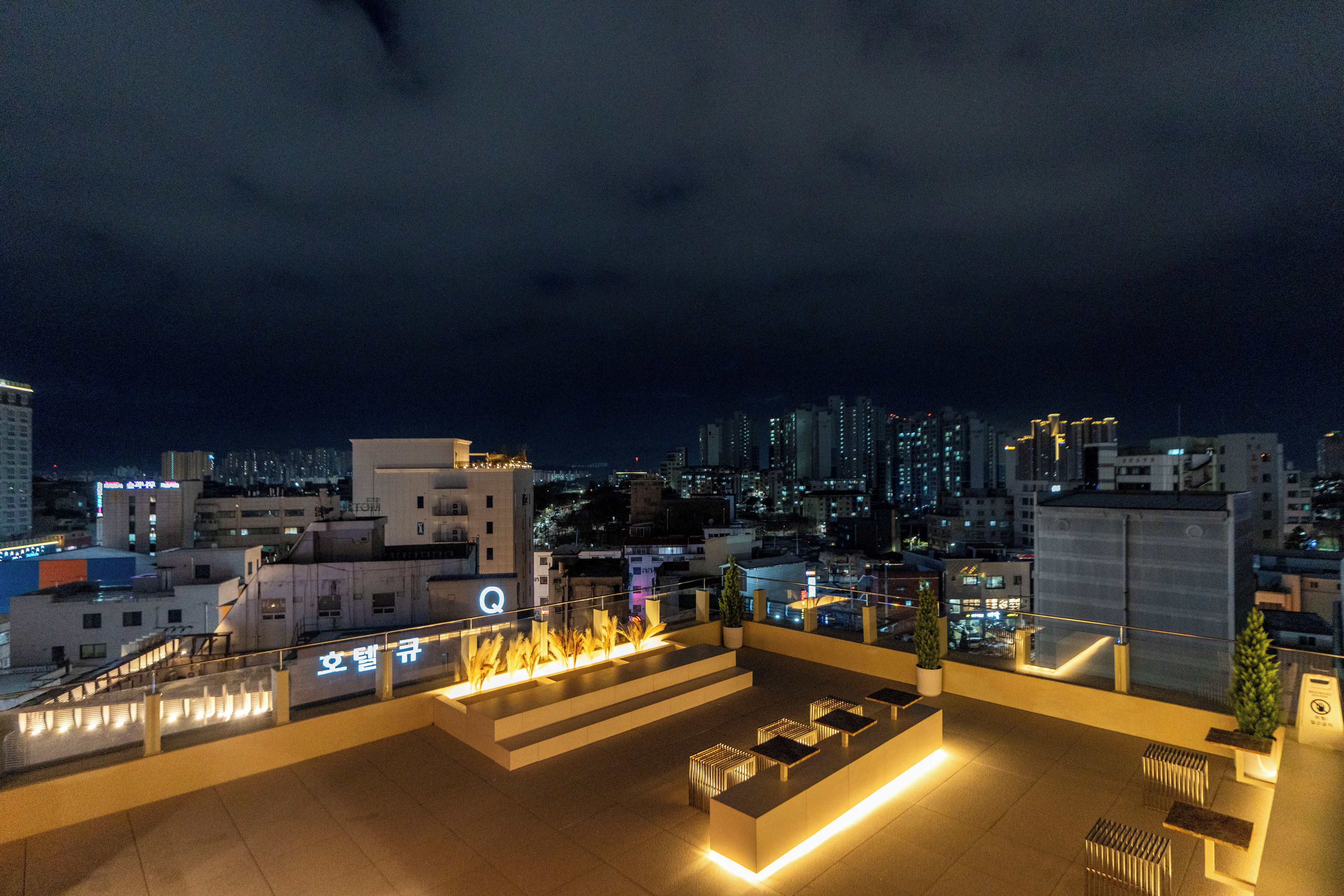 Una terraza en la azotea con una chimenea, zonas de estar y vistas de la ciudad iluminada por la noche.
