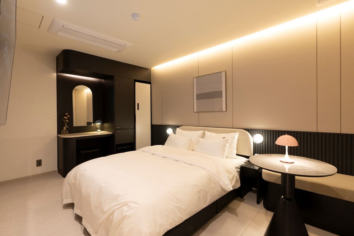A modern bedroom with a large bed, bedside tables, a round table, and a mirror.