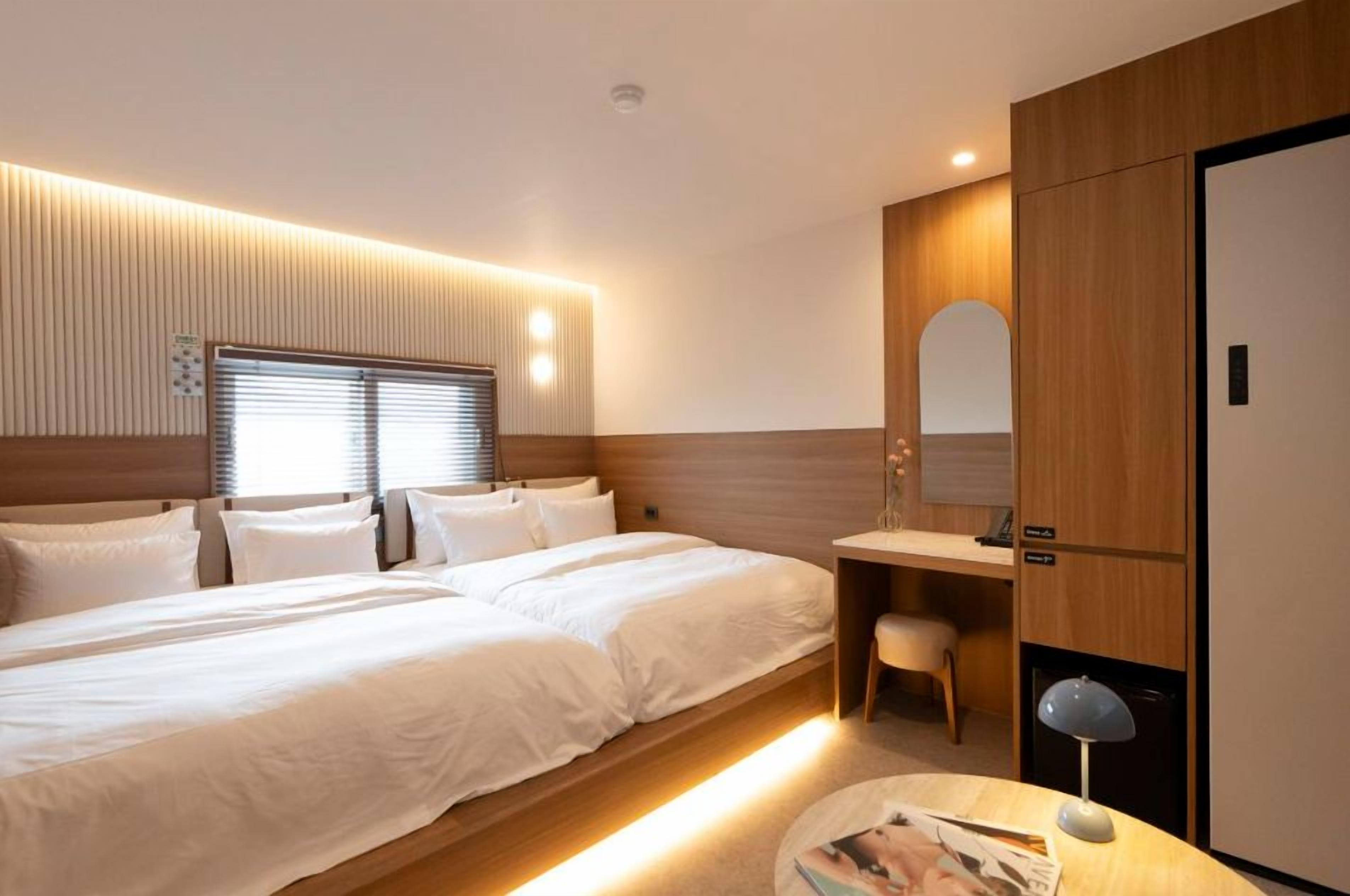 Ett hotellrum med en stor säng, ett skrivbord, en stol och en spegel.