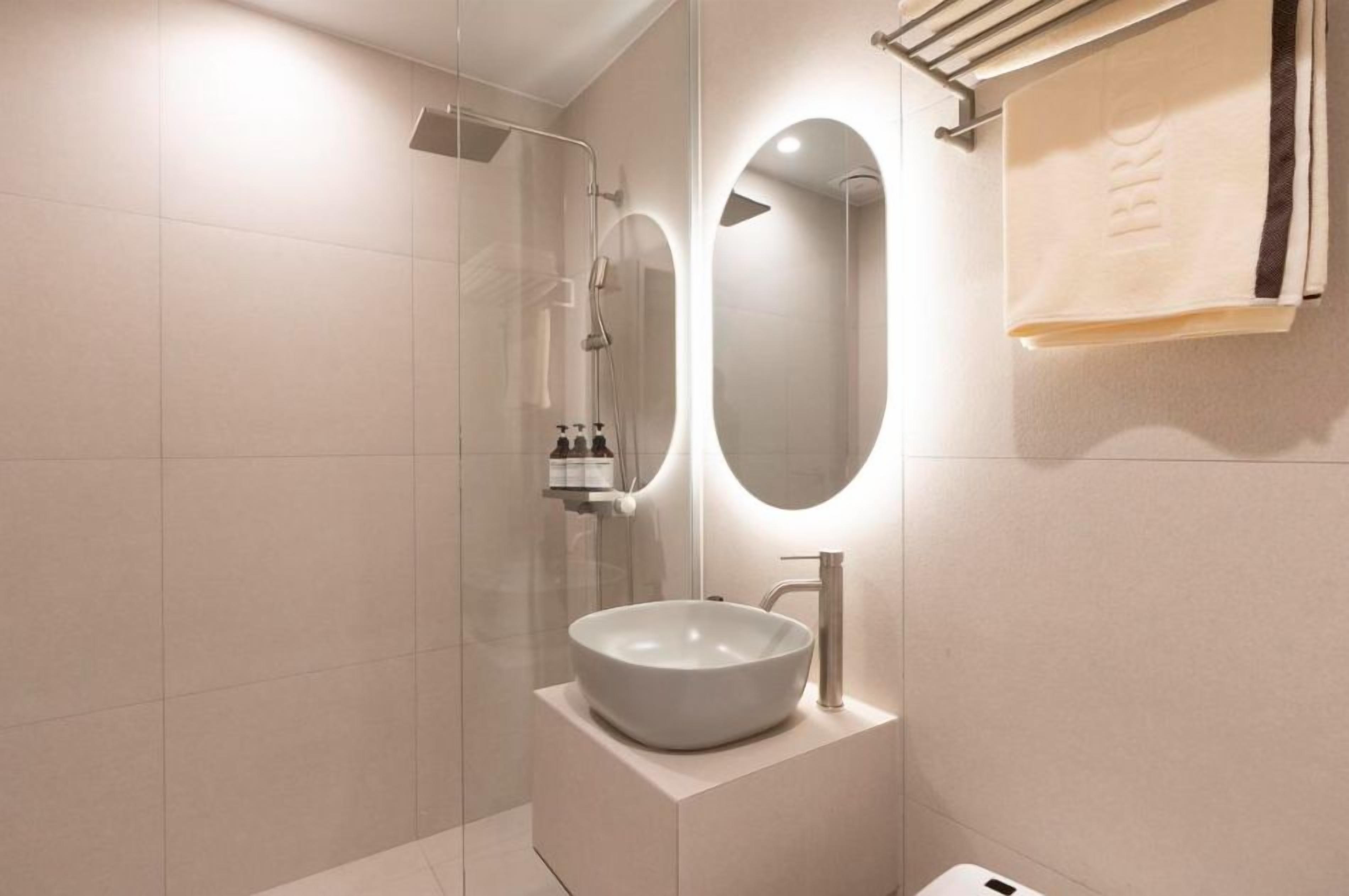 A modern bathroom with a glass-enclosed shower, a round mirror, and a white sink.
