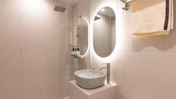 A modern bathroom with a glass-enclosed shower, a round mirror, and a white sink.