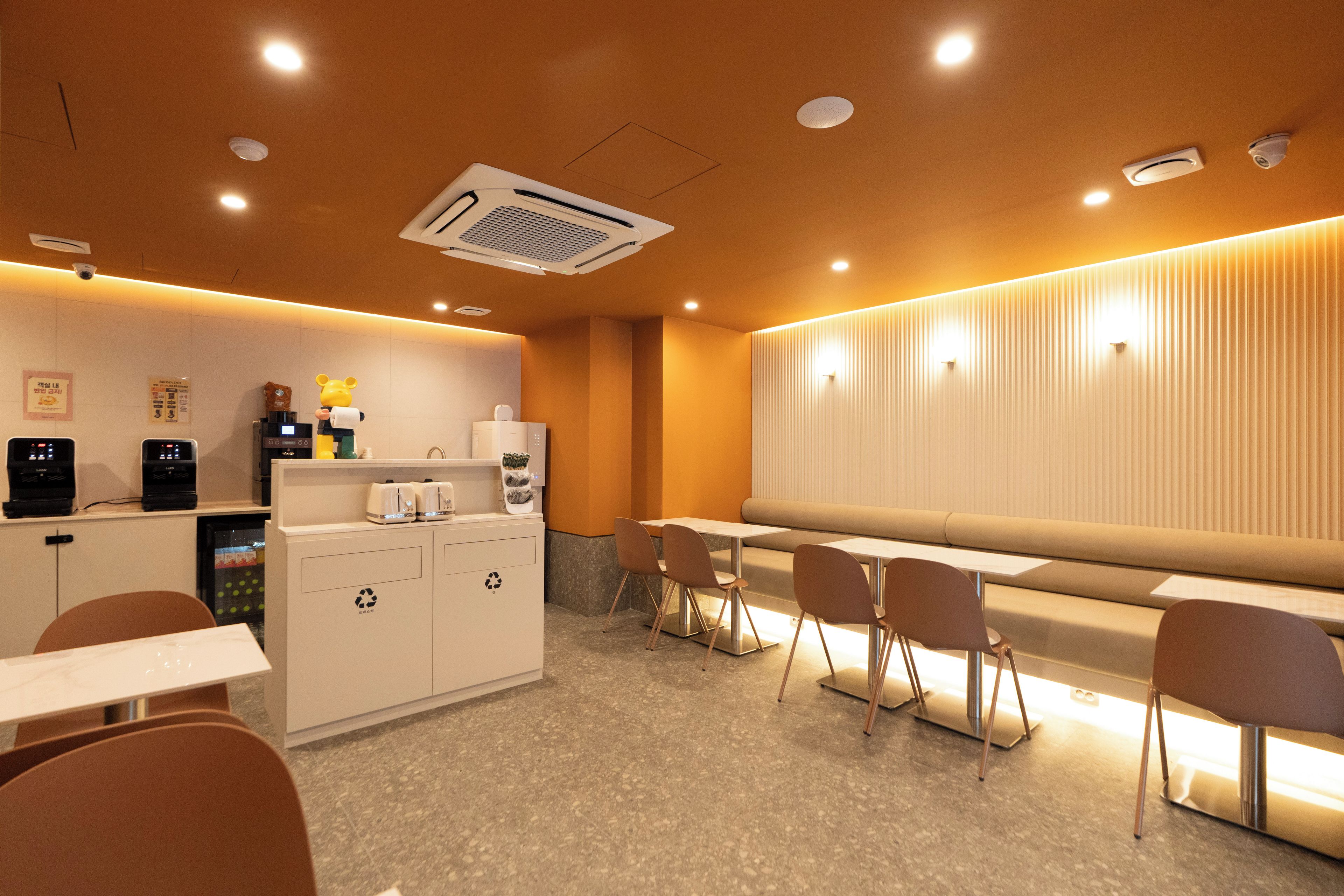 A modern cafe with a seating area, a counter with coffee machines, and a recycling bin.