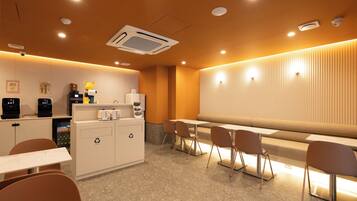 A modern cafe with a seating area, a counter with coffee machines, and a recycling bin.