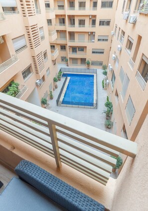 A multi-story residential building with a central courtyard featuring a swimming pool. - Spacious 3-Bedroom Apartment • Pool, Balcony, and Free Parking (Marrakech)