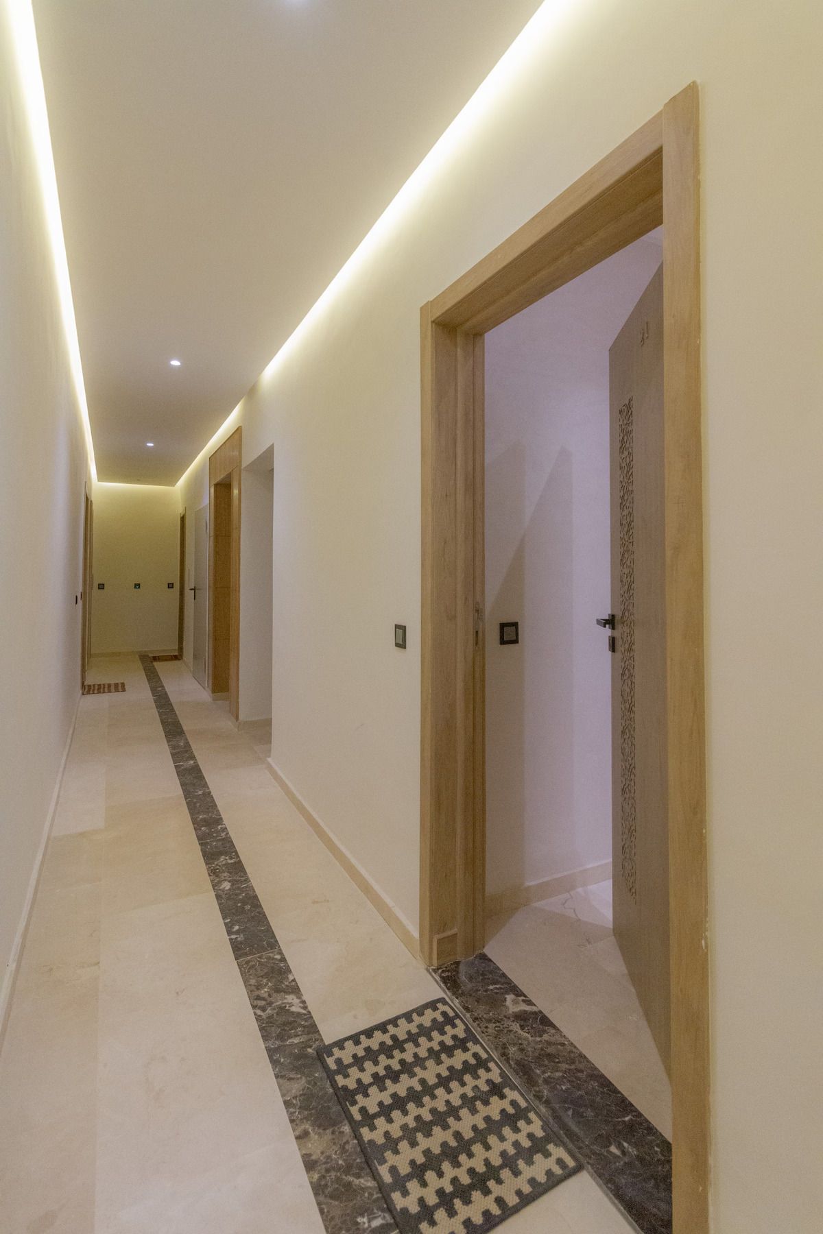 A corridor with wooden doors, a patterned rug, and a tiled floor.