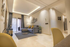 A modern living room with a sofa, coffee table, and chairs. There is a staircase leading to another level. - Spacious 3-Bedroom Apartment • Pool, Balcony, and Free Parking (Marrakech)