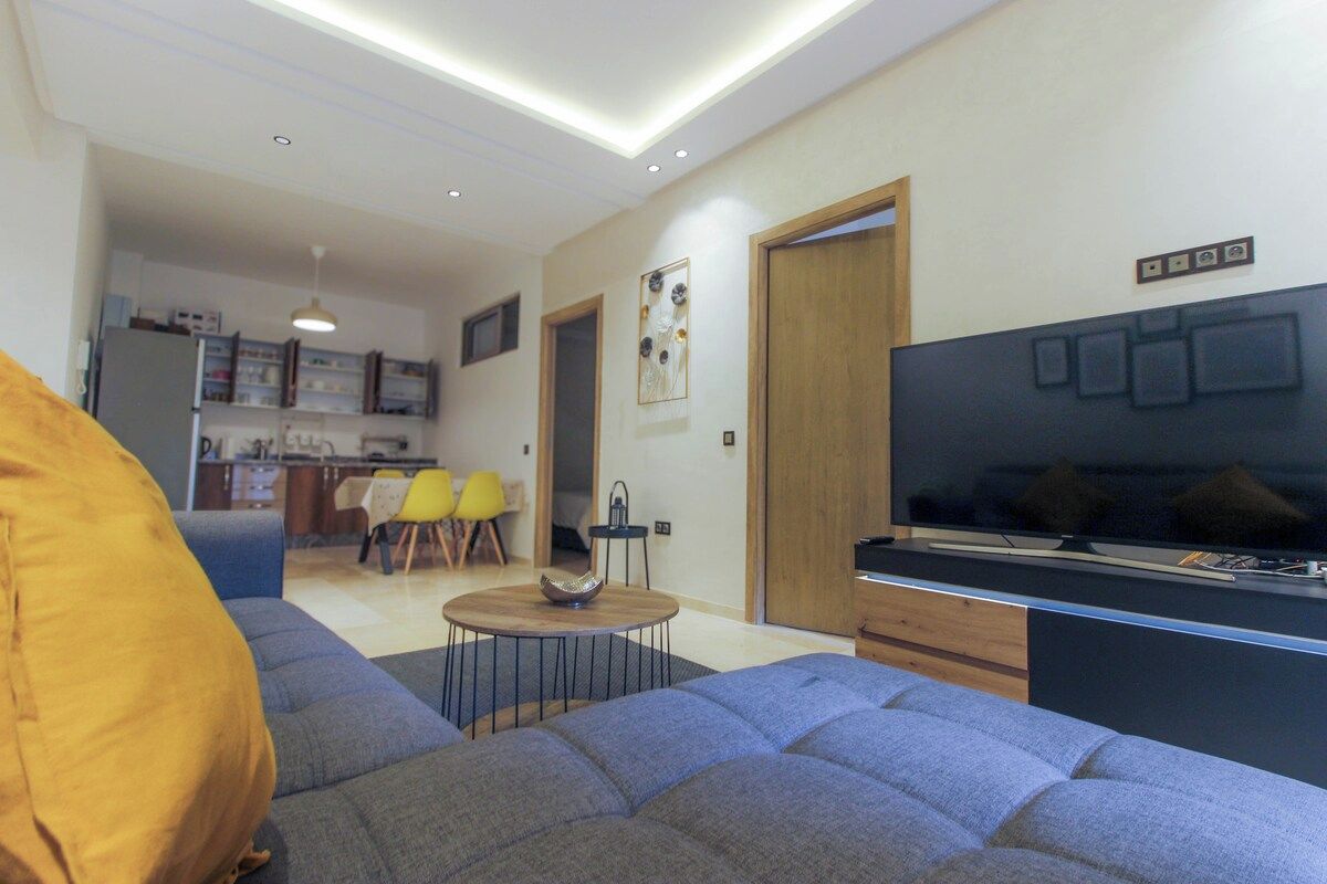 A modern living room with a sofa, a TV, and a dining area with chairs and a table.