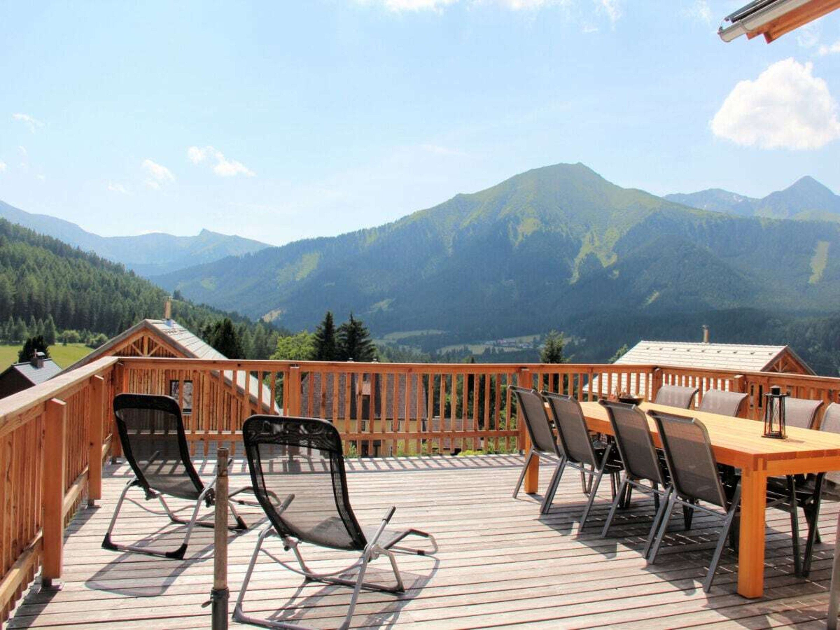 A wooden deck with a table and chairs overlooking a mountainous landscape.