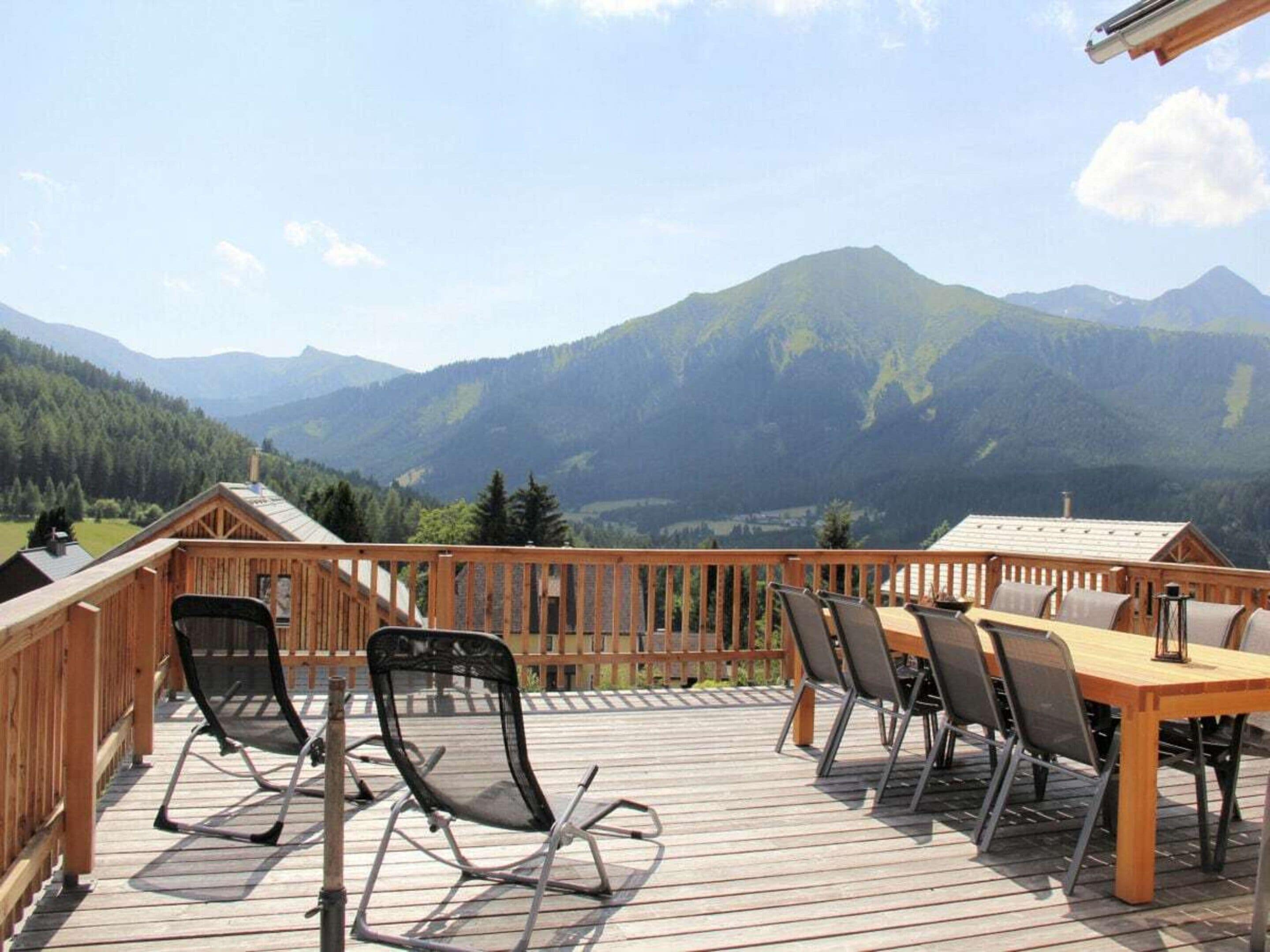 Een houten terras met tuinmeubilair met uitzicht op een bergachtig landschap.