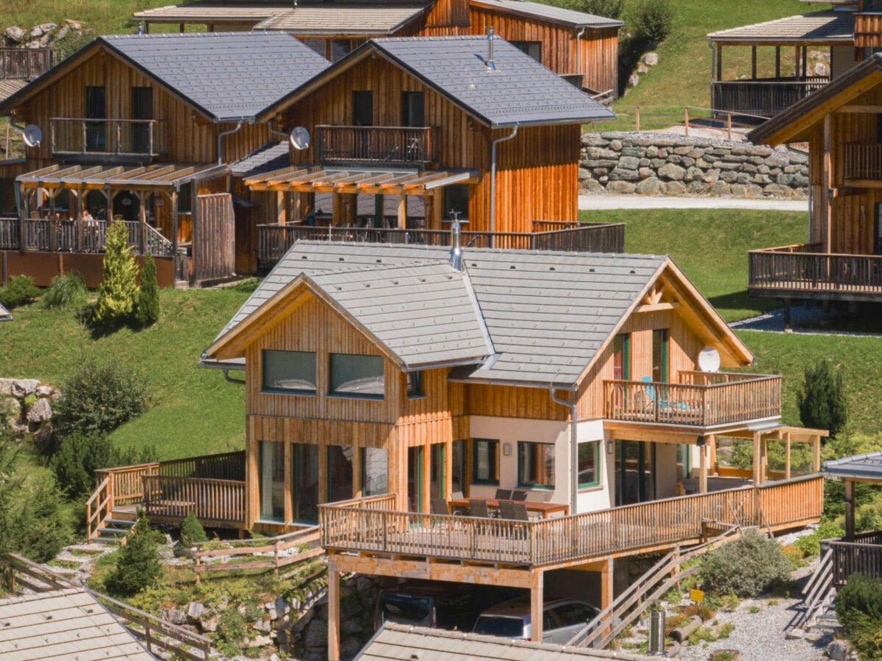A cluster of wooden cabins with balconies, a covered outdoor seating area, and a stone wall in the background.