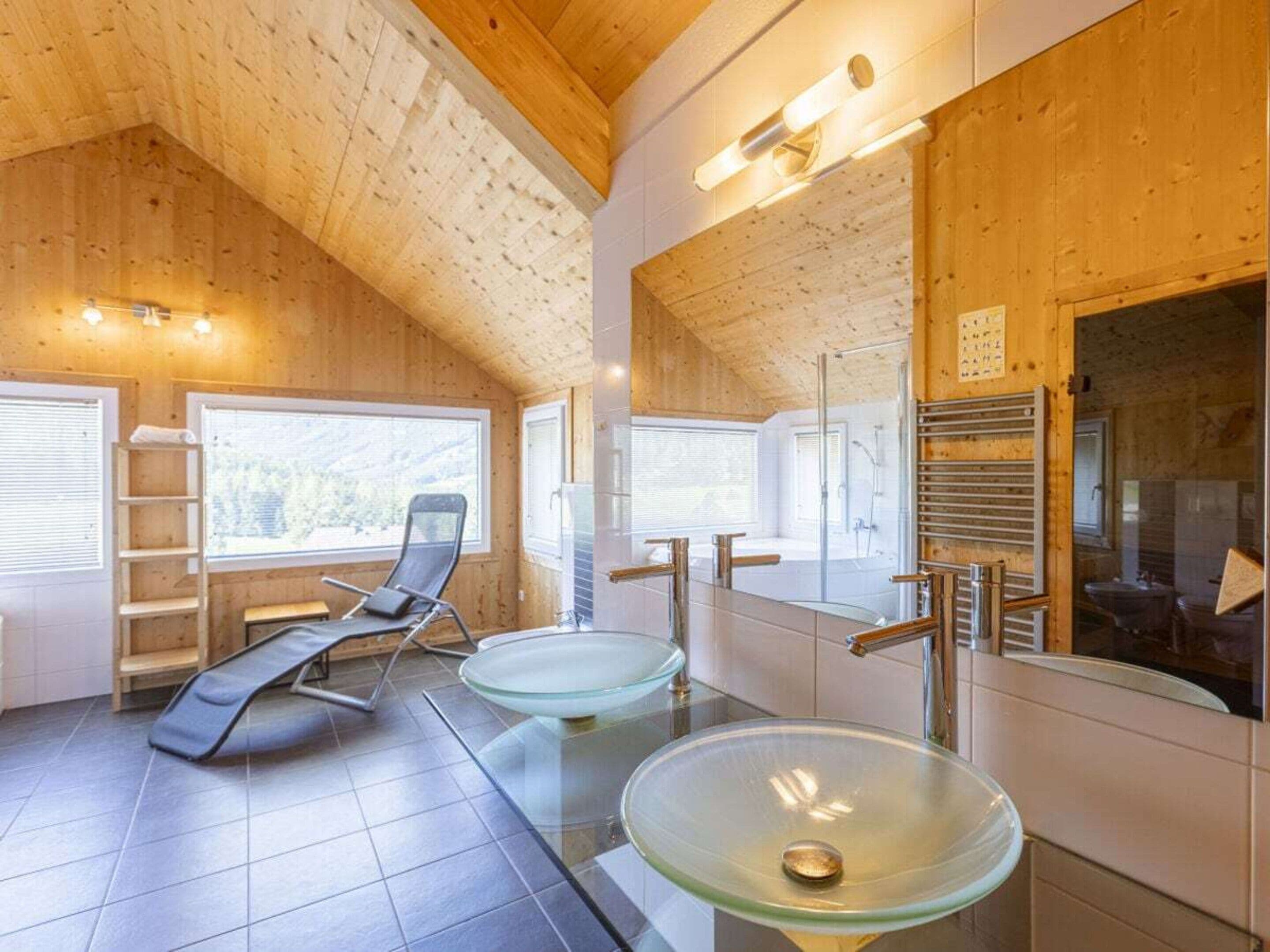 A modern bathroom with a glass sink, a bathtub, and a shower. There is a chair and a ladder against the wall.