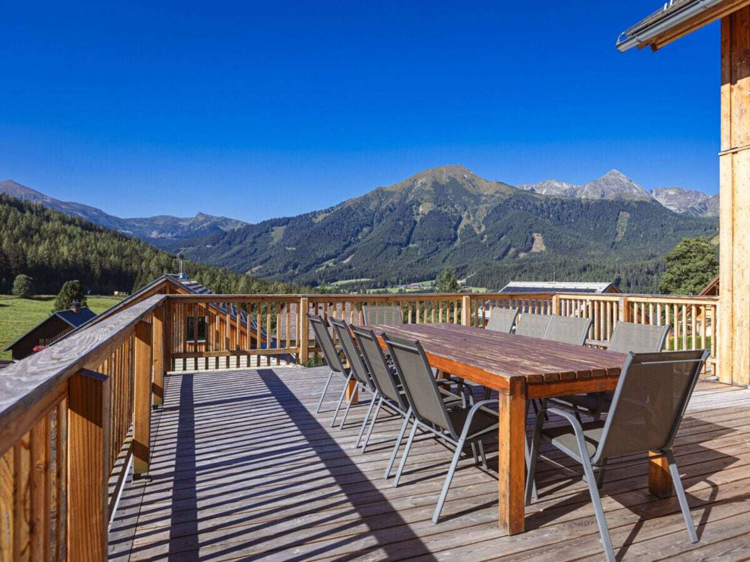 A wooden deck with a table and chairs, overlooking a mountainous landscape.