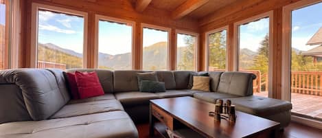 A modern living room with a sectional sofa, a coffee table, and large windows offering a mountain view.