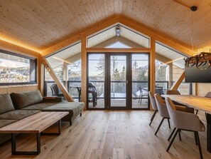 A modern interior with a wooden ceiling, a dining area with a table and chairs, a sofa, and a large sliding glass door leading to an outdoor deck. - Superior Chalet # 7 With Sauna & Hot Tub (Stadl-Predlitz)
