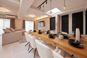 A modern dining area with a long wooden table, white chairs, and a flat-screen TV mounted on the wall. - eni.taniroku (Osaka)