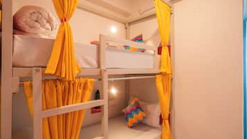 A bunk bed room with yellow curtains, a pillow, and a small table with a water bottle.