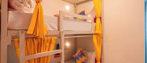 A bunk bed room with yellow curtains, a pillow, and a small table with a water bottle.