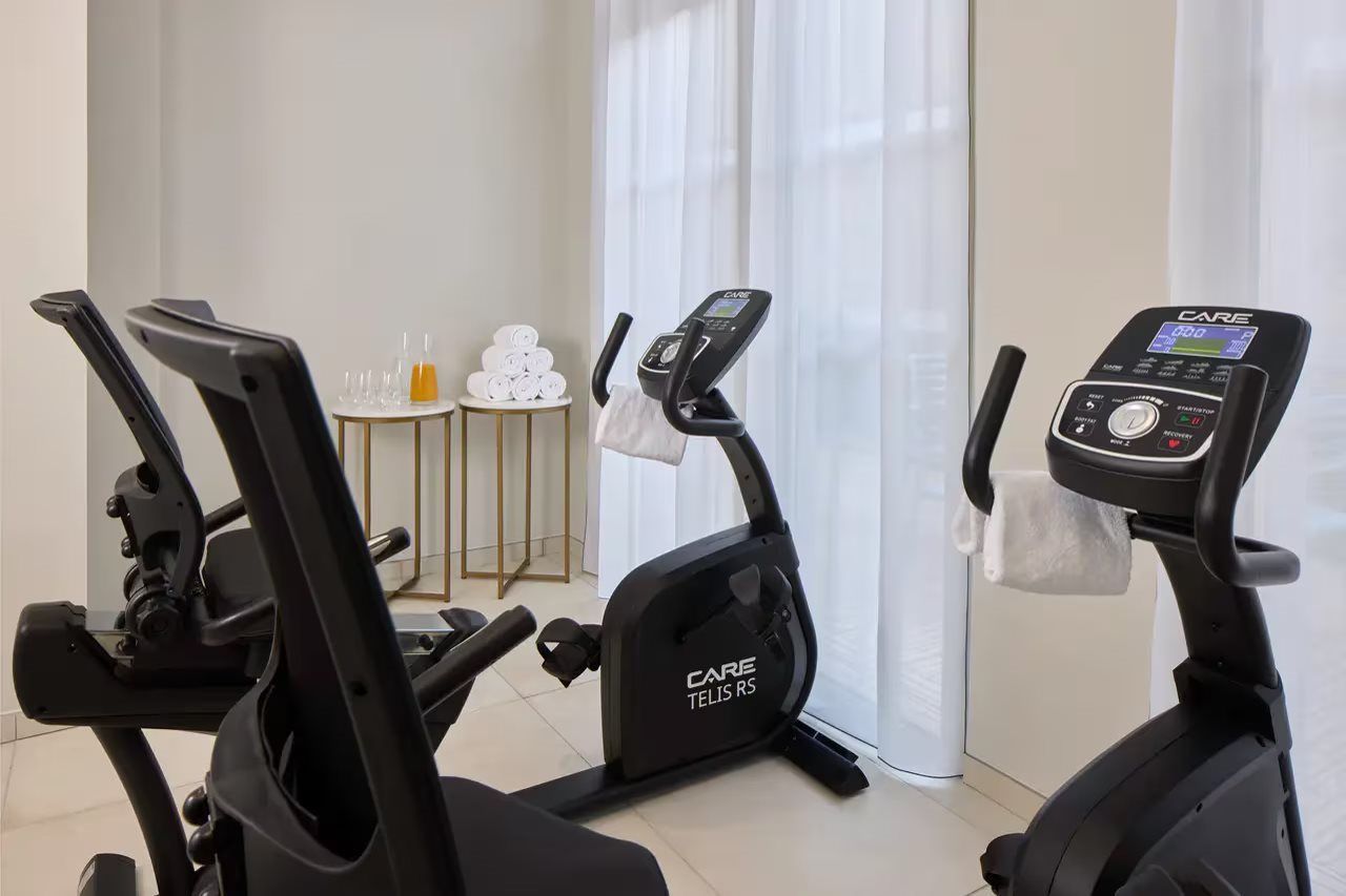 A home gym with two stationary bikes, a small table with towels, and a window with curtains.