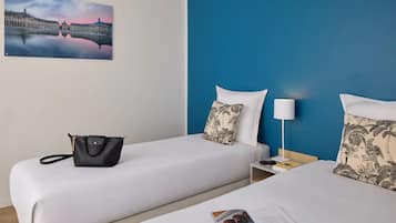A hotel room with two beds, a nightstand, a lamp, a black handbag, and a framed picture on the wall.