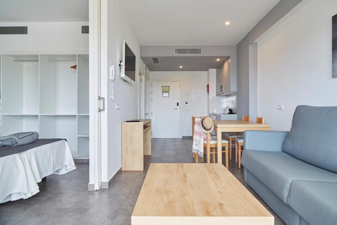 A modern living room with a sofa, a coffee table, a dining area with a table and chairs, a kitchen in the background, and a walk-in closet with shelves.
