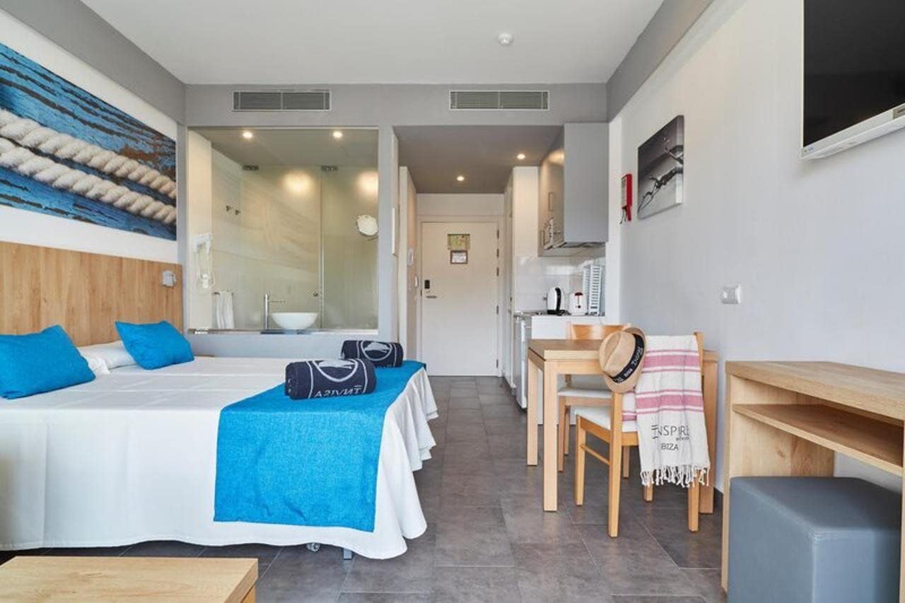 A hotel room with a bed, a desk, a chair, and a small table.