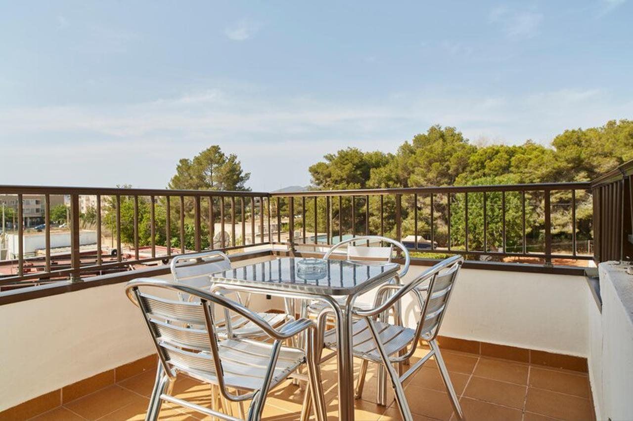 A balcony with a glass table and metal chairs, overlooking a residential area with trees and buildings.