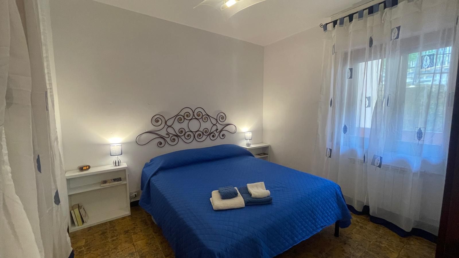 Une chambre à coucher avec un lit, deux tables de chevet, une horloge murale et une fenêtre avec des rideaux.