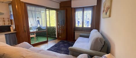Una habitación con cama, sofá, una mesita y ventana con cortinas.