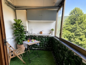 A small balcony with artificial grass, a wooden chair, a table with a white tablecloth, and potted plants. - Bauhouse - Apartment between the sea and the mountains; pets allowed. (Chiose)