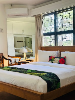 Een hotelkamer met een bed, nachtkastje, lamp, raam met geometrisch patroon en uitzicht op buiten.